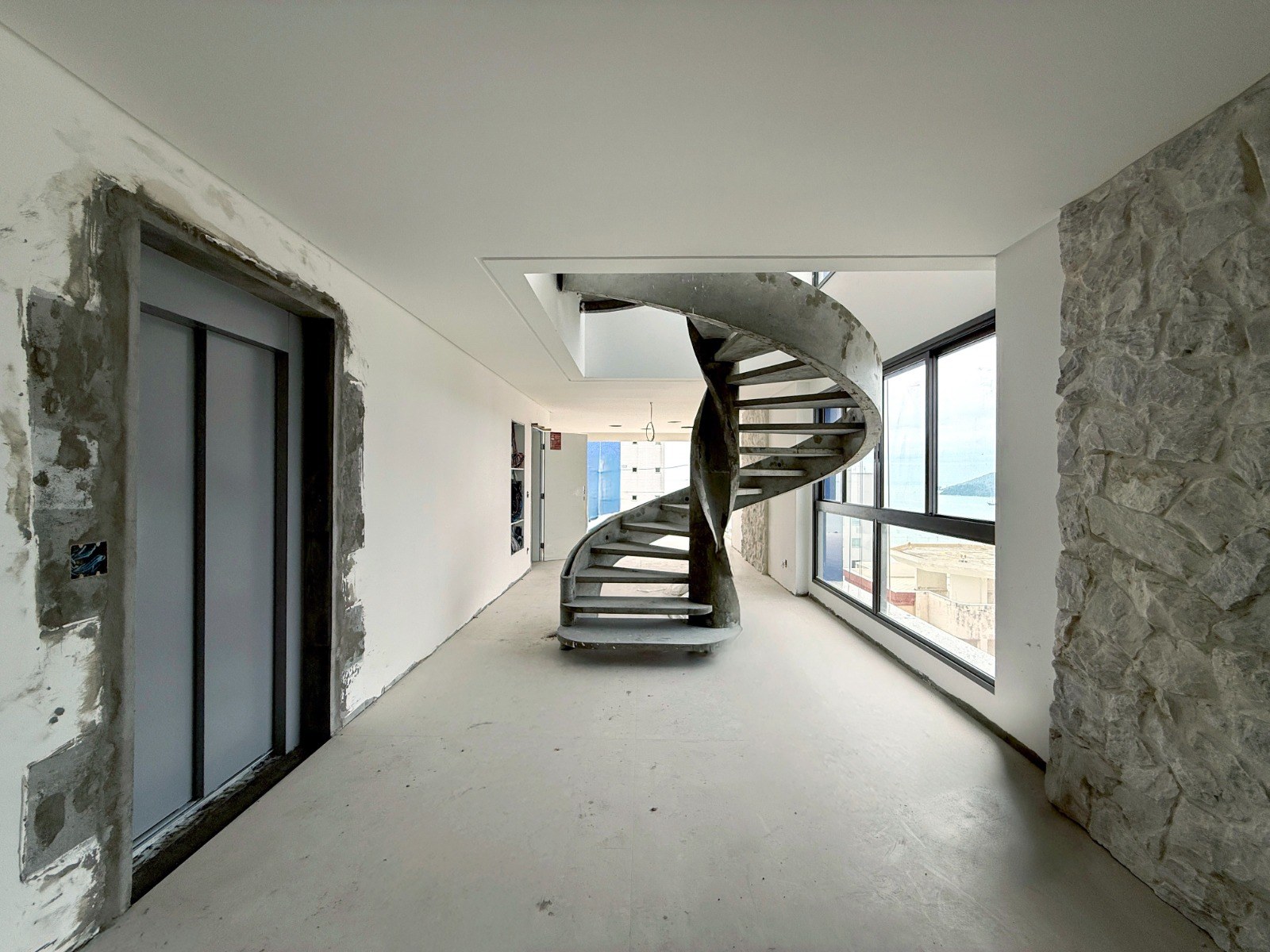 Apartamento em fase de obra com escada helicoidal e parede de pedra